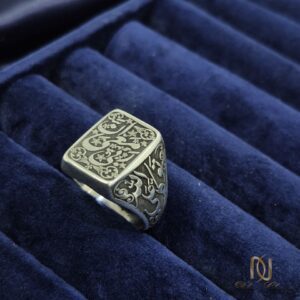انگشتر نقره مردانه طرح مهر ان معی ربی | کد محصول ri-m-6 | عکس روی نمایشگر مخمل آبی، نمای زاویهای از روی صفحه مربعی با حکاکیهای کتیبه فارسی و اسلیم