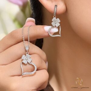 نیم ست نقره جواهری طرح قلب و گل چهارپر ce-new-83، مدل زنانه با پوشش گوشواره و دست در حال نگه داشتن گردنبند