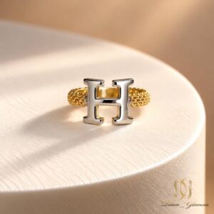انگشتر نقره زنانه شیک حرف H | کد محصول ri-s-102 | نمای ایستاده روی پایه نمایش سفید با پس زمینه گرم